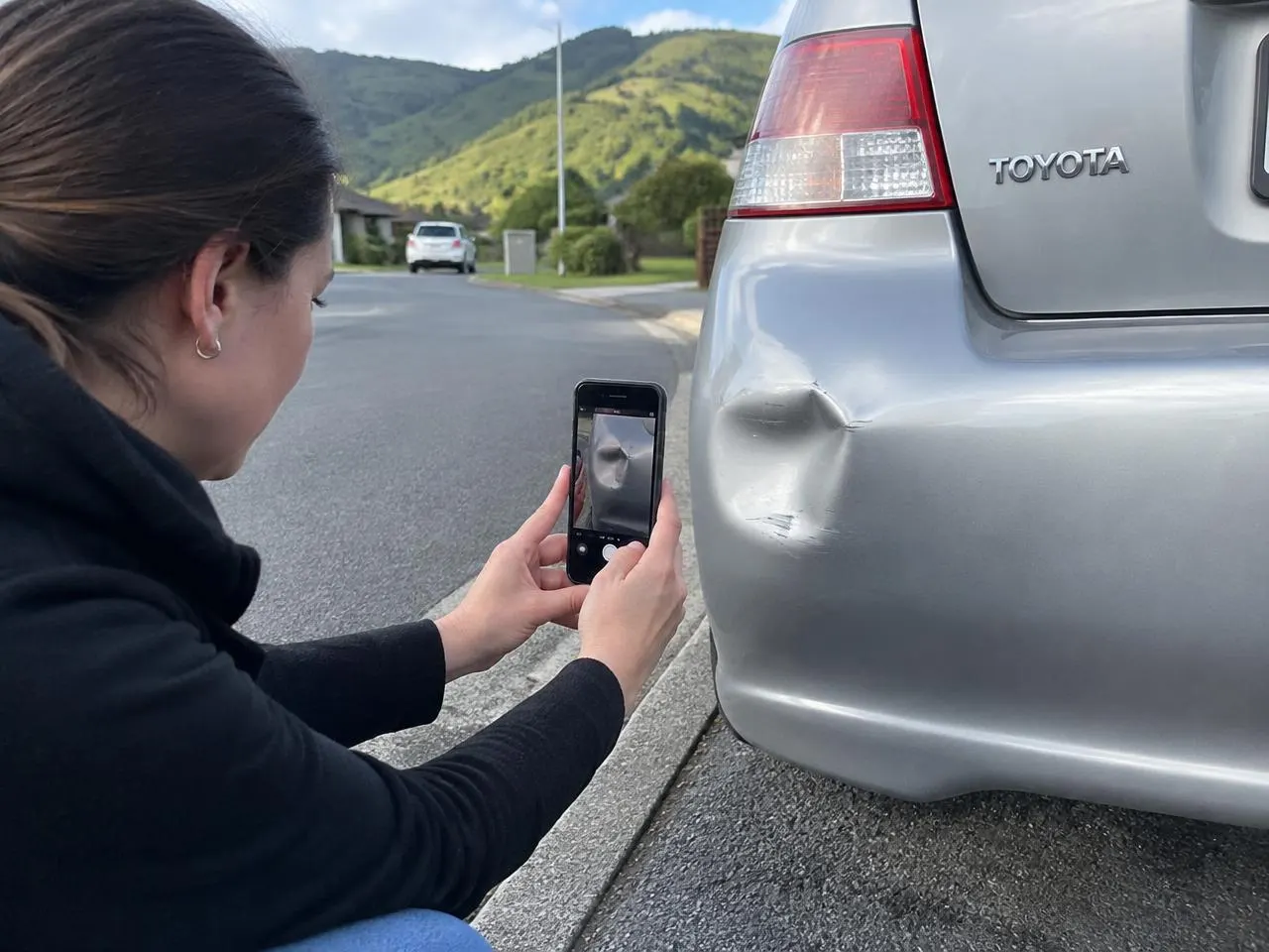 Driver photographing a dented bumper with a phone